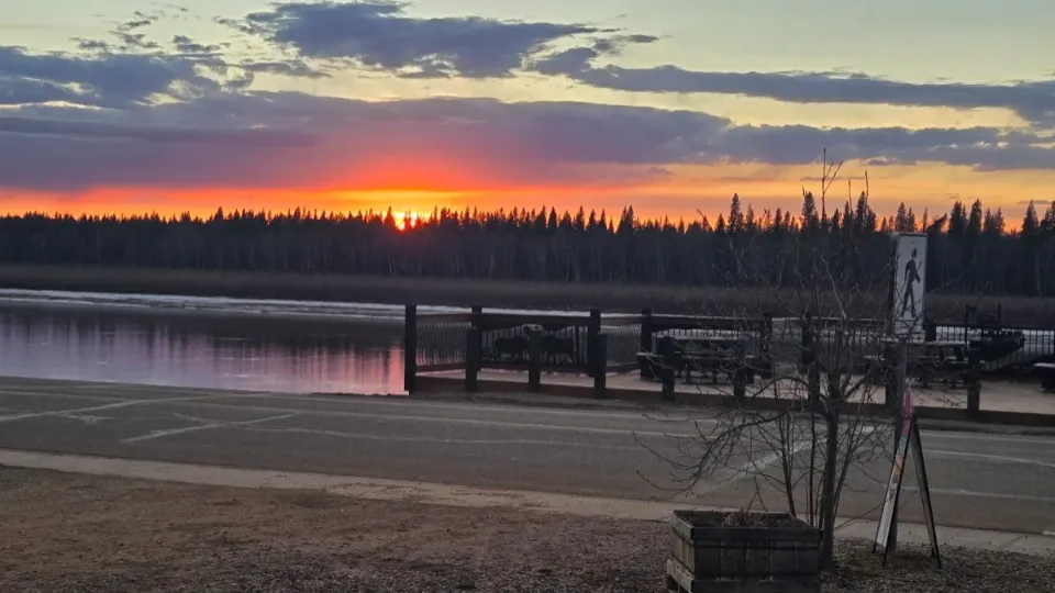 Wooden deck with picnic tables overlooking the Peace River at sunset, across from The Harvest Table in Fort Vermilion
