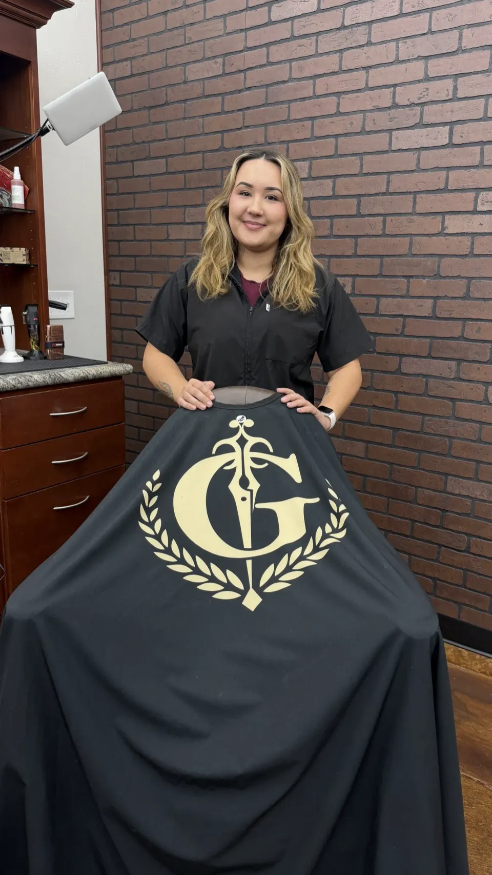 Mariah holding the black Gentlemen's Cutz cape with the gold crest