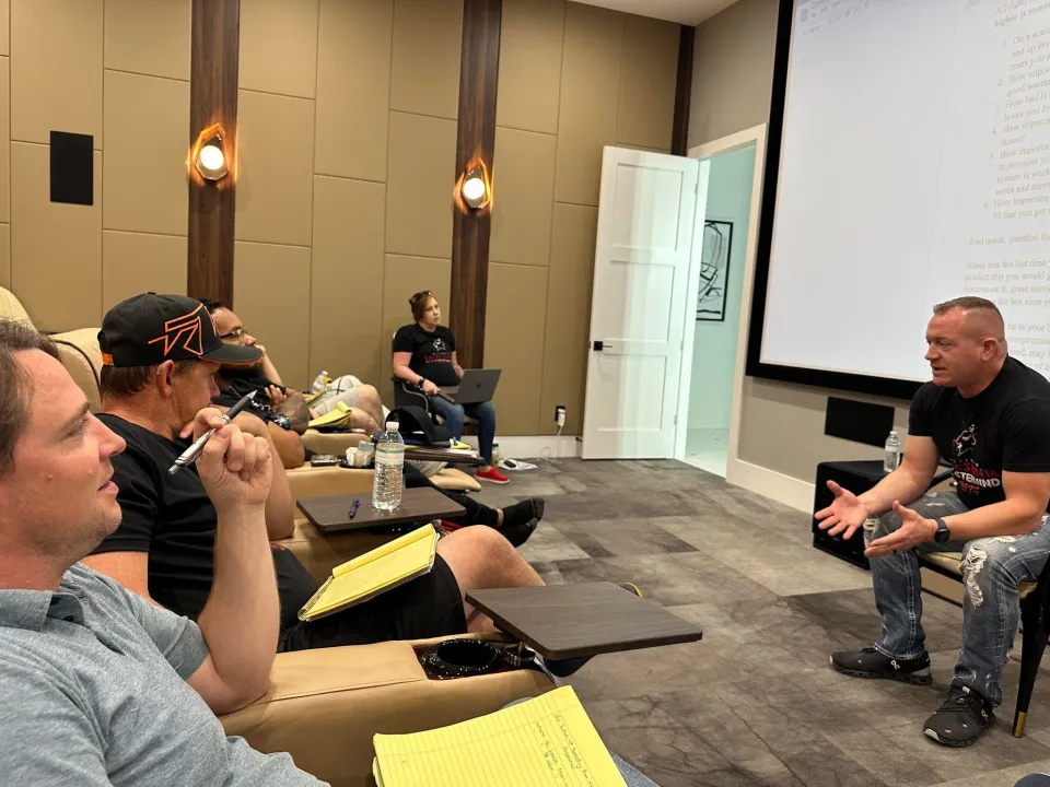 Gene Slade sits facing a group of seated trainees with notepads in a home theater room
