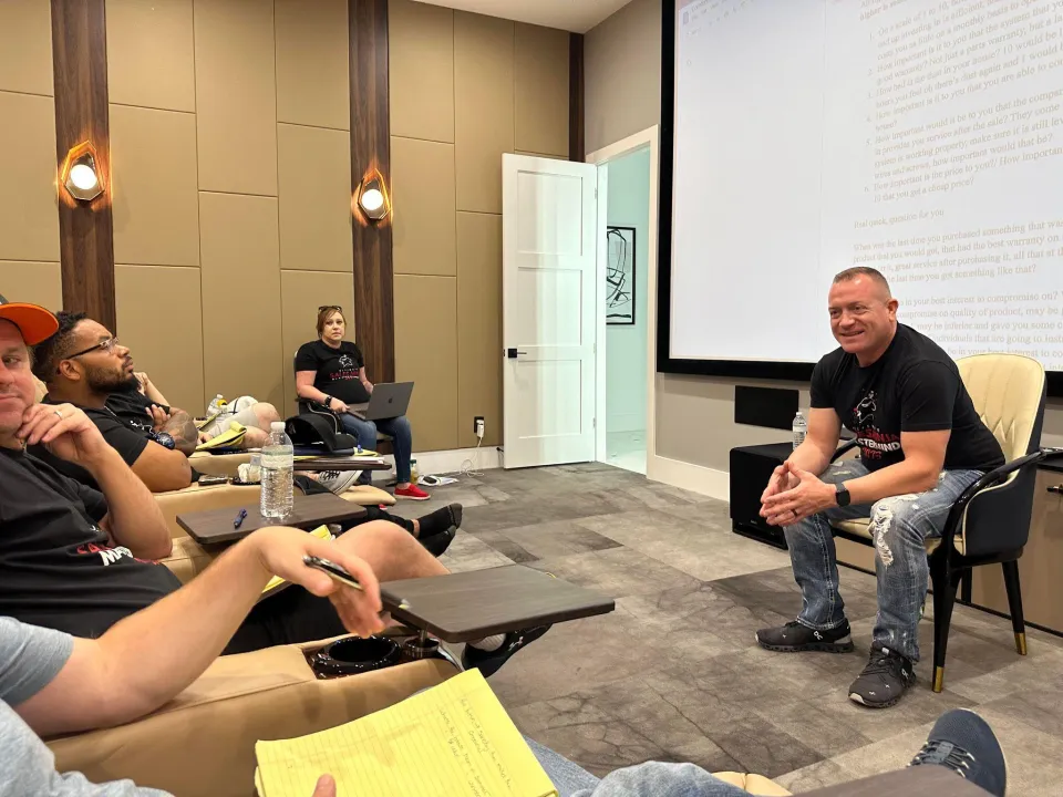 Wide view of a training room with trainees seated facing Gene Slade and a projector screen