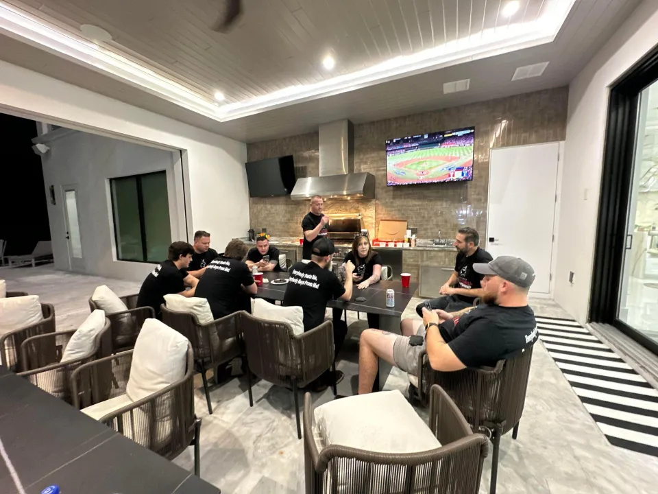 Owners and technicians sit around a long table in a large house kitchen