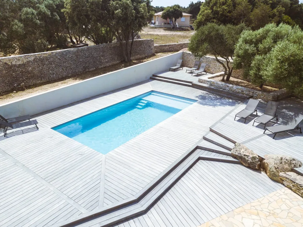 Piscine coque dans un jardin corse avec terrasse, murs en pierre et végétation méditerranéenne