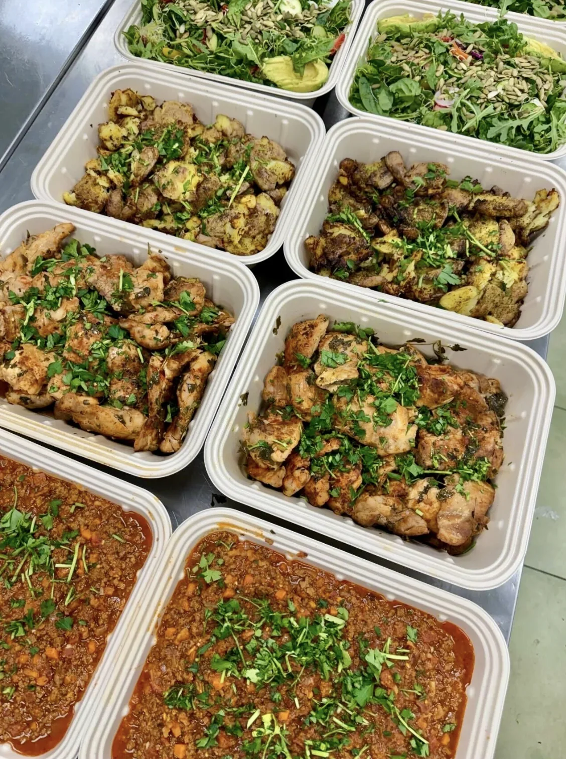 Catering pans of grilled chicken, greens and beef bolognese ready for a team meal