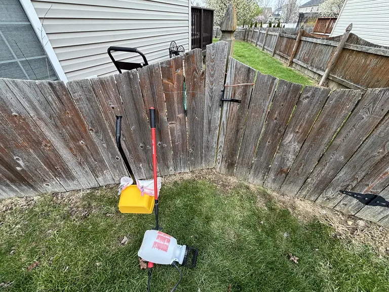 Wood backyard gate with cleanup tools beside a green side yard.