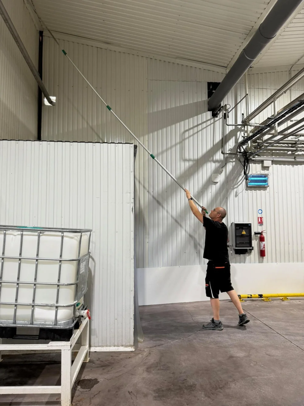 Nettoyage à la perche des parois et de la charpente intérieure d'un atelier de production, site en activité
