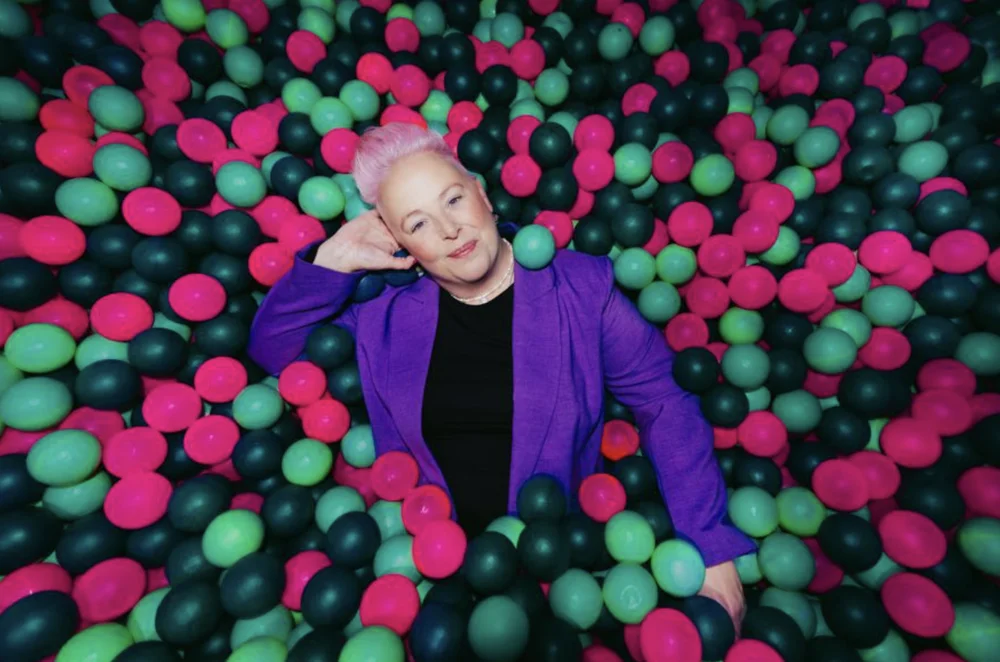 Suzi Payton smiling while lying back in a pink and green ball pit