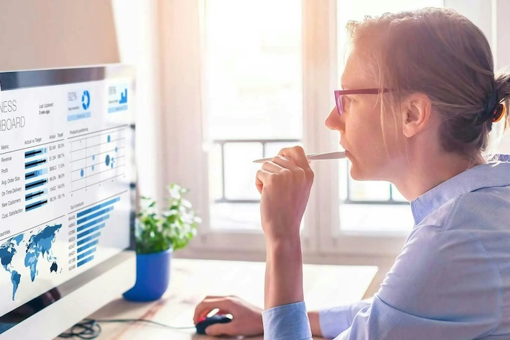 Woman biting pen, looking at computer dashboard.