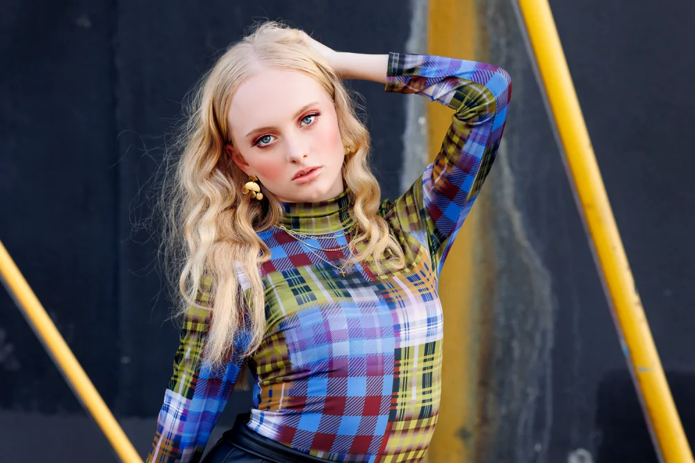 High School Senior Girl in plaid patterned top against a black wall with yellow accents