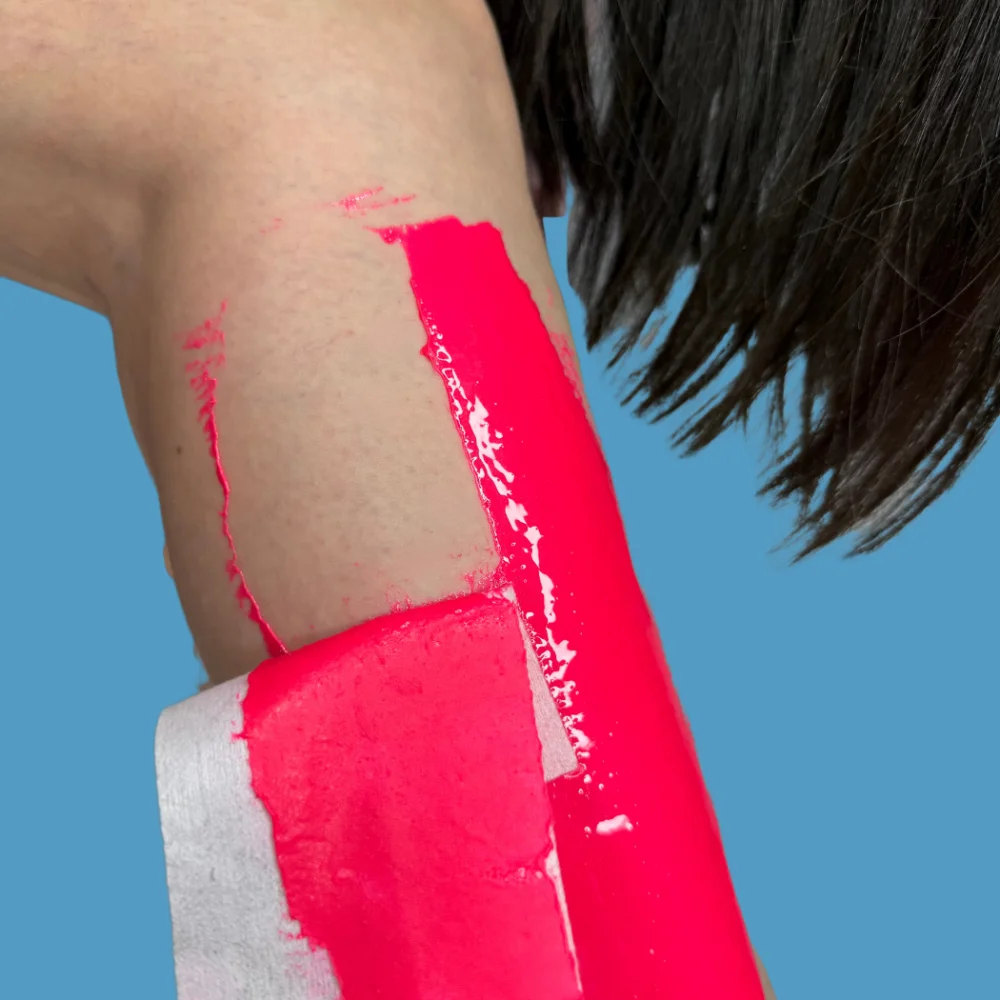 Dragonfruit Pink sugar paste spread on leg with strip removing it. Long hair of women hanging in background