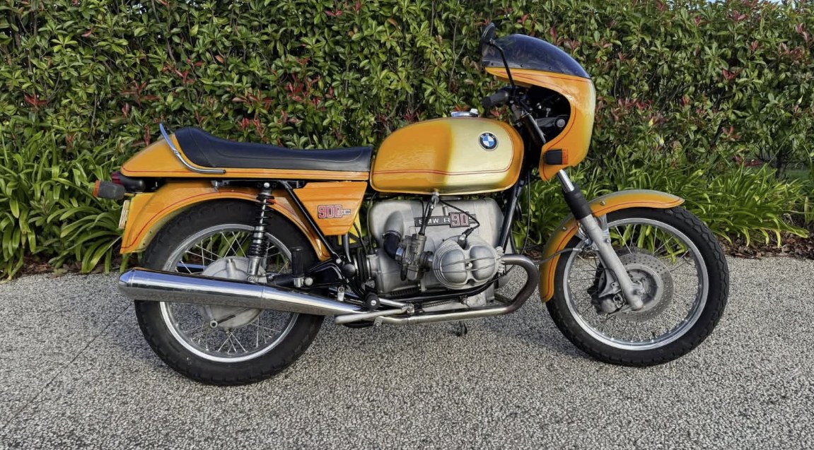 Orange 1970s BMW 900 parked in front of a hedge