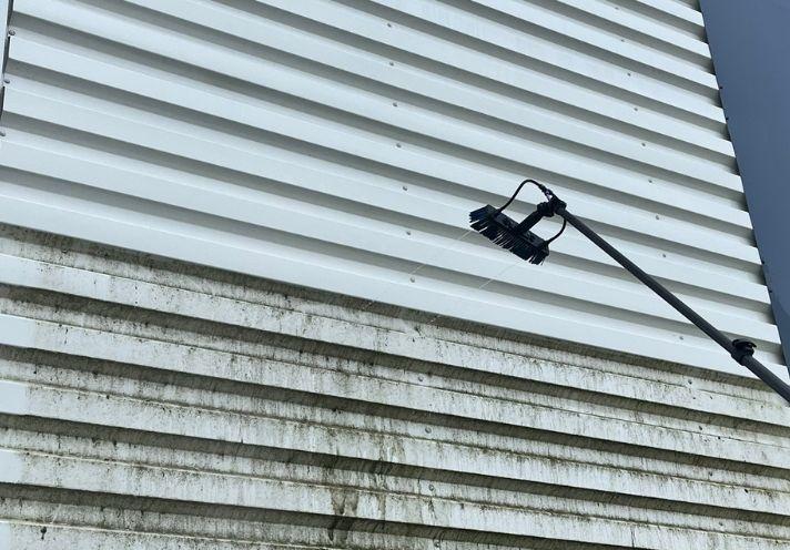 Bardage industriel en cours de nettoyage : la partie haute est redevenue blanche, la partie basse reste couverte de dépôts verts et noirs