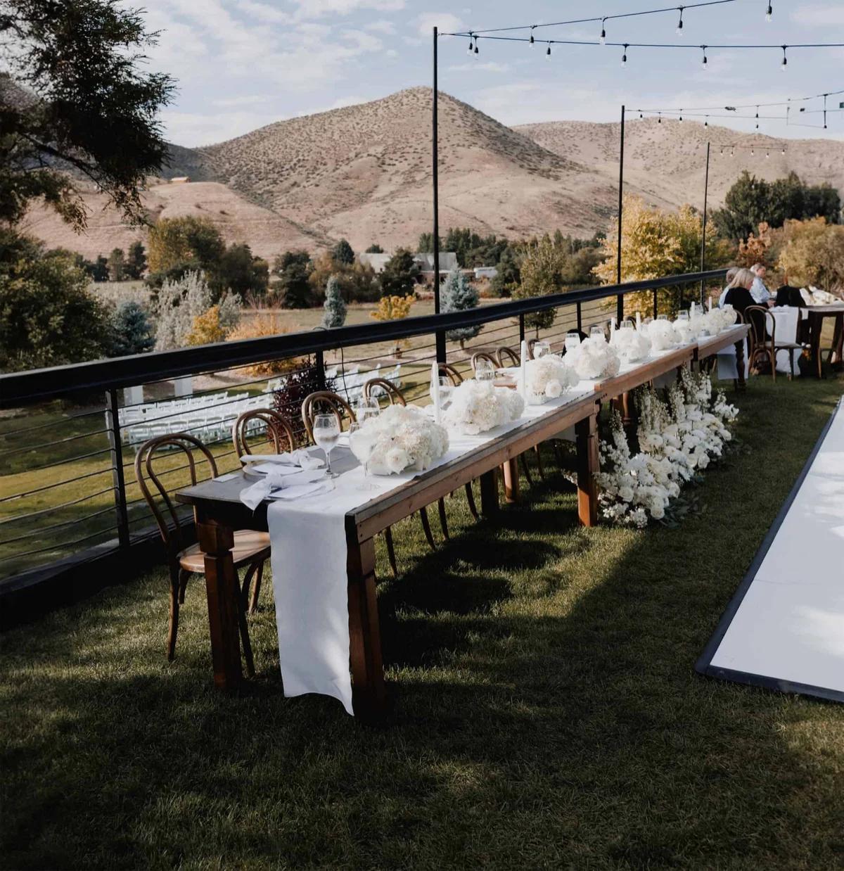 Long outdoor table set beneath string lights with foothill views