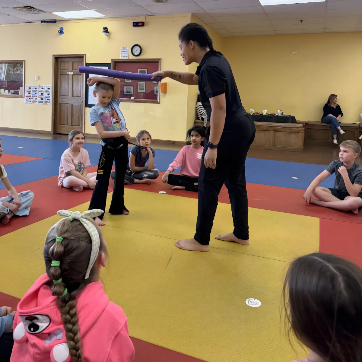 Mastery instructor holding a breaking board for a child while the other guests watch