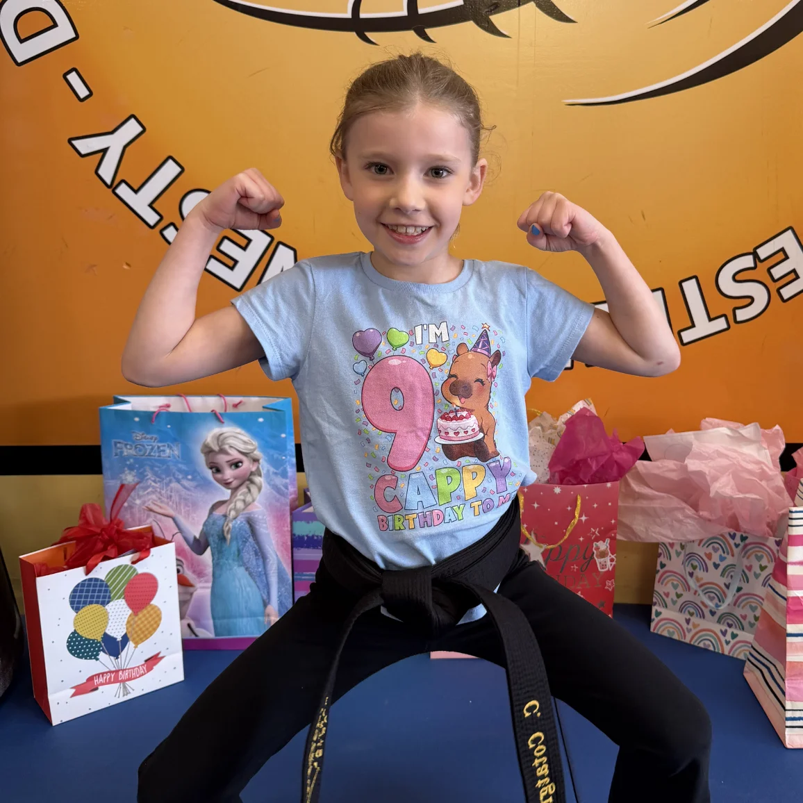 Birthday girl in her Mastery Martial Arts uniform flexing beside her birthday presents