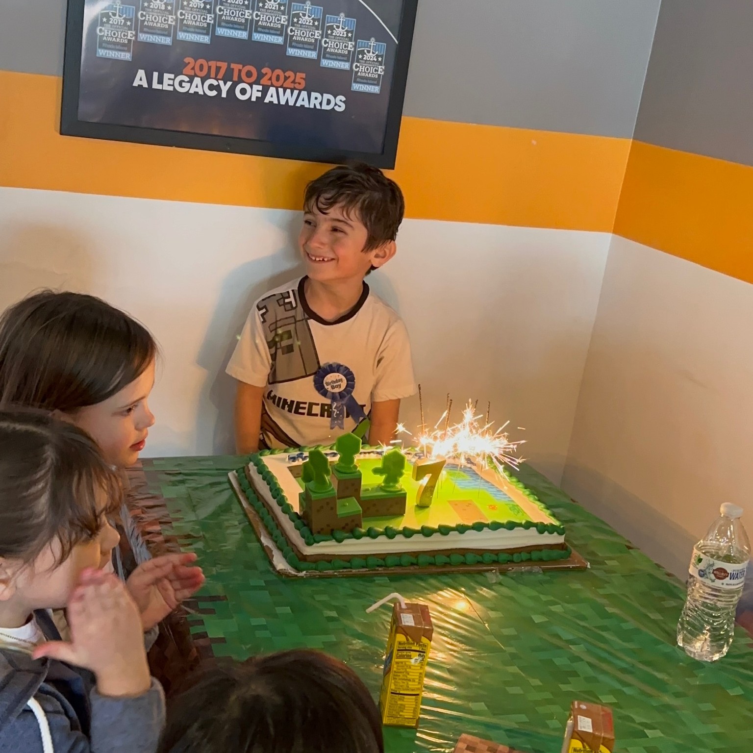 Birthday boy behind his sparkler-lit birthday cake surrounded by cheering friends