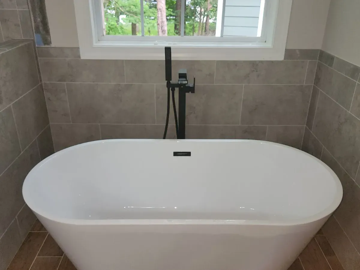 Freestanding tub with floor-mount black faucet in a remodeled bathroom