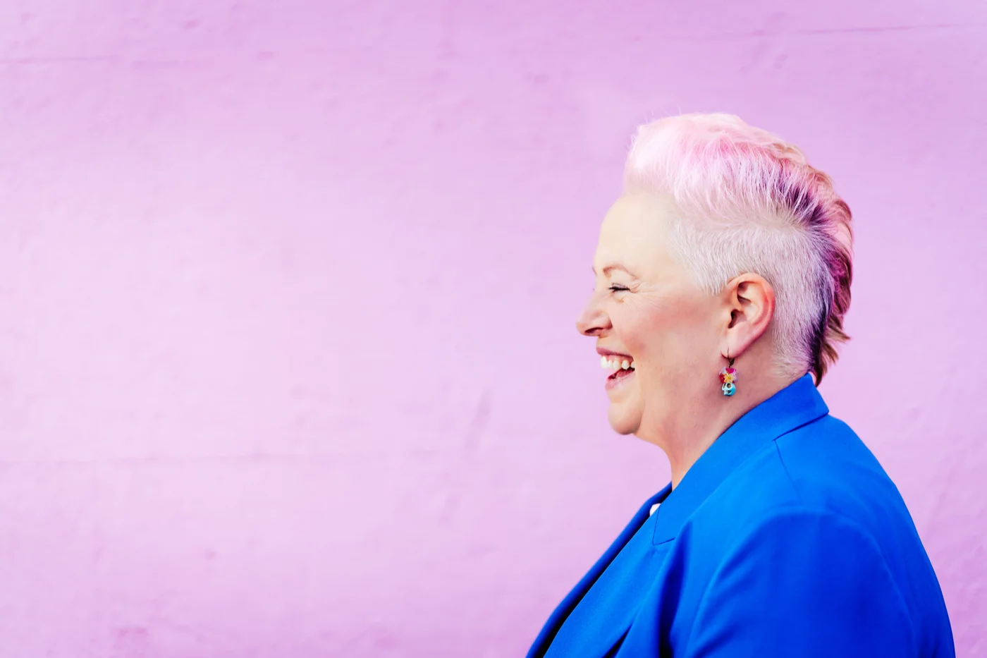 Suzi Payton laughing in profile against a lilac wall