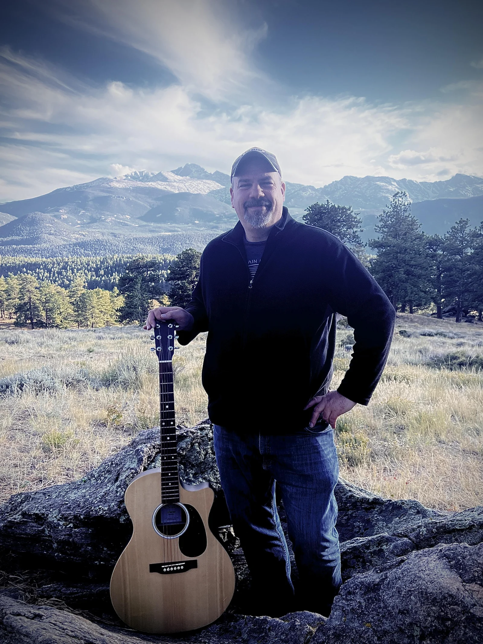 Ted Gaunt standing with his acoustic guitar in the Colorado mountains