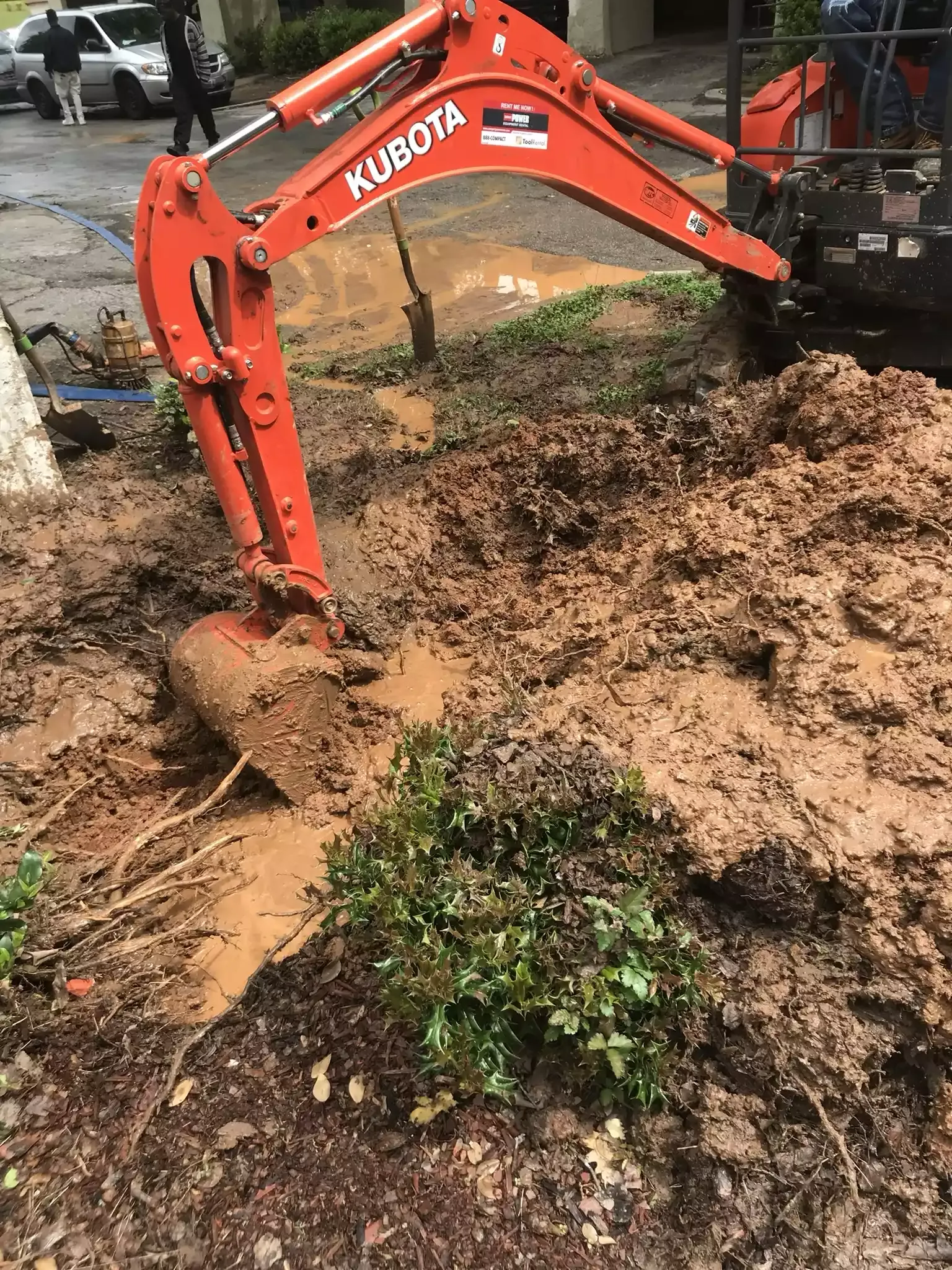 Compact excavator digging a plumbing trench in a front yard