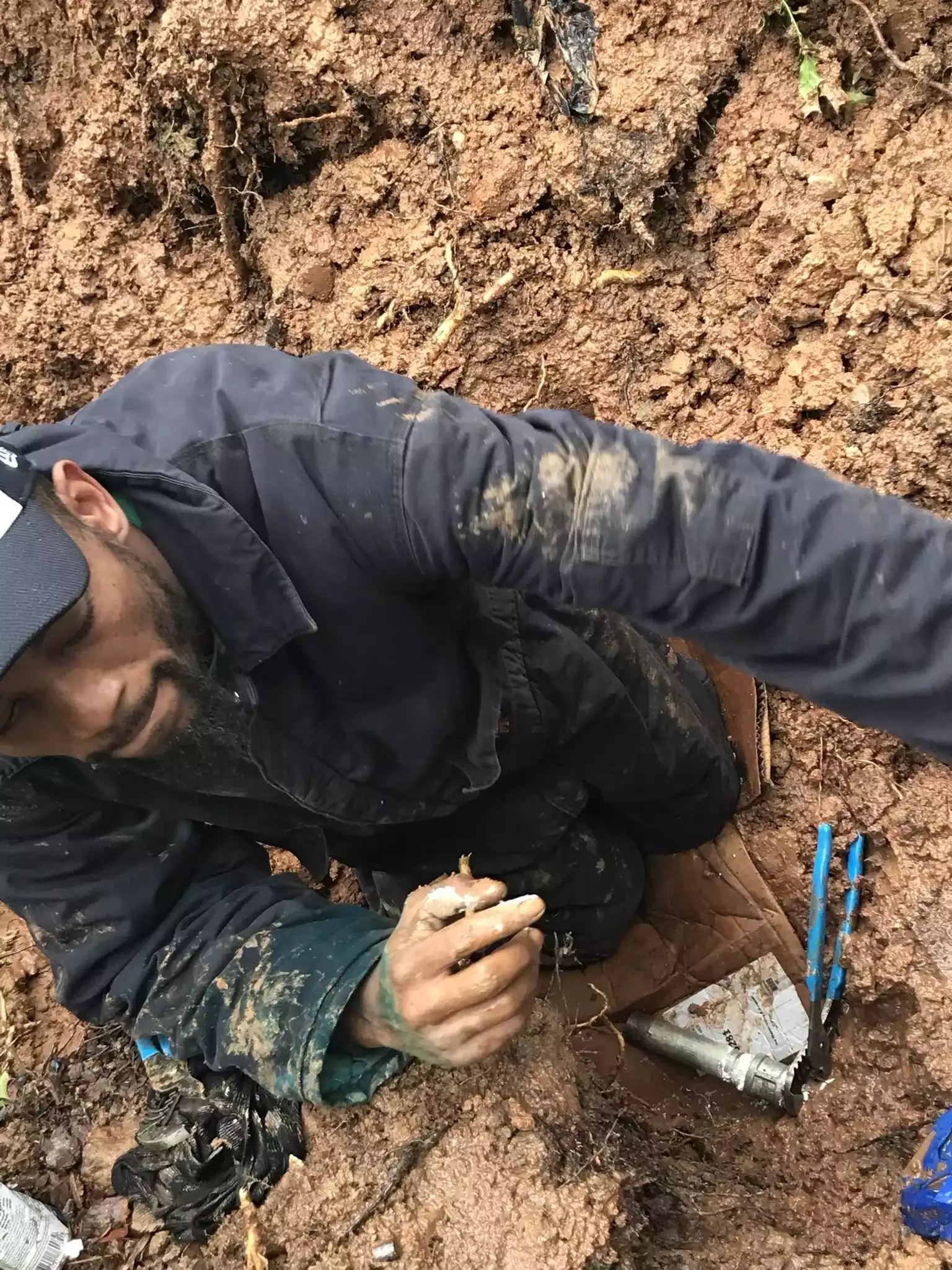 Plumber repairing a broken water line in an open trench