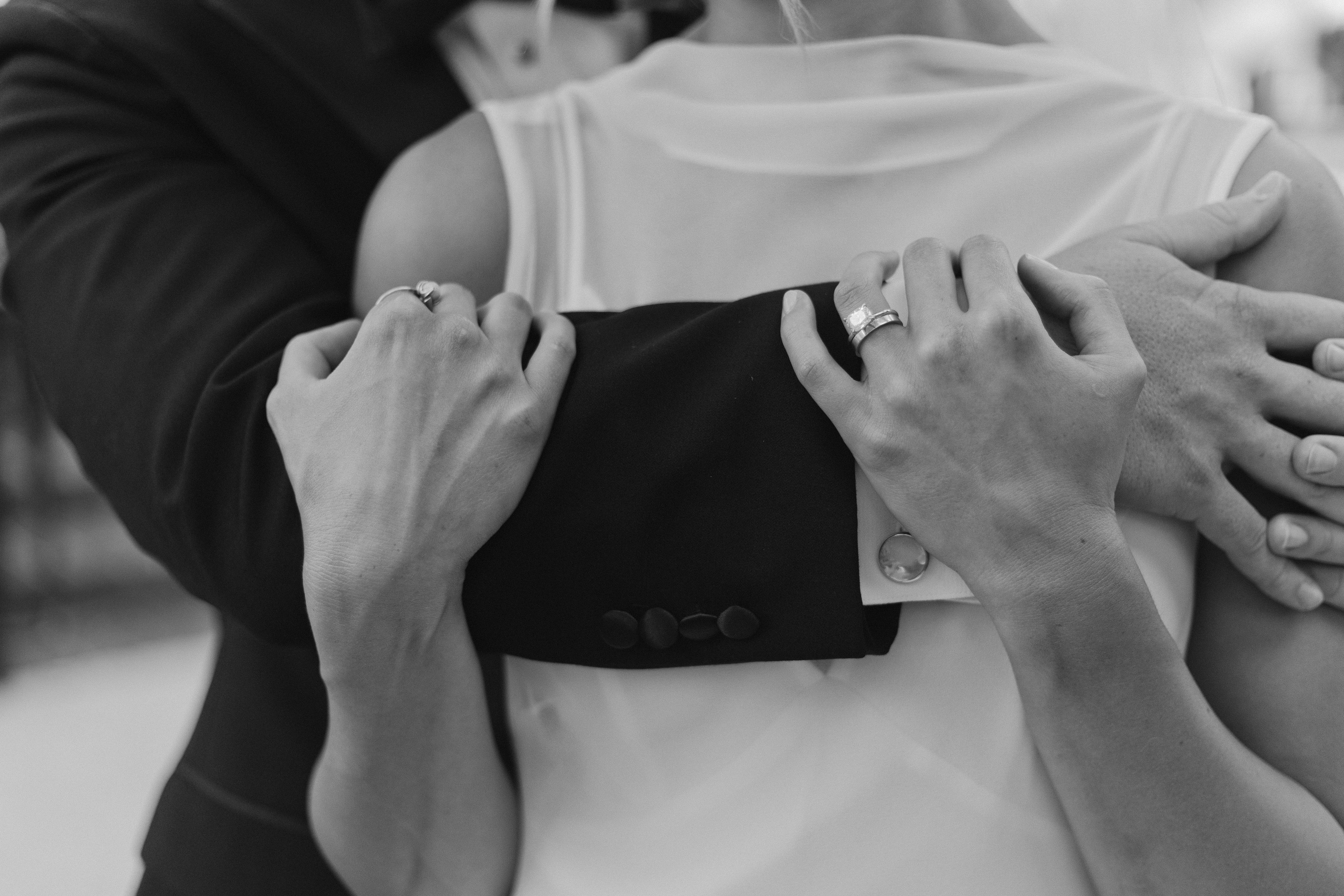 Black and white detail of a bride and groom embracing, wedding rings visible