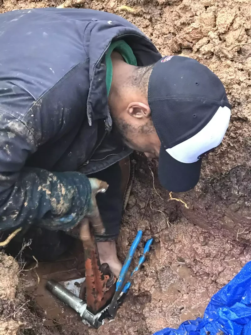 Technician hand digging to expose a damaged sewer pipe