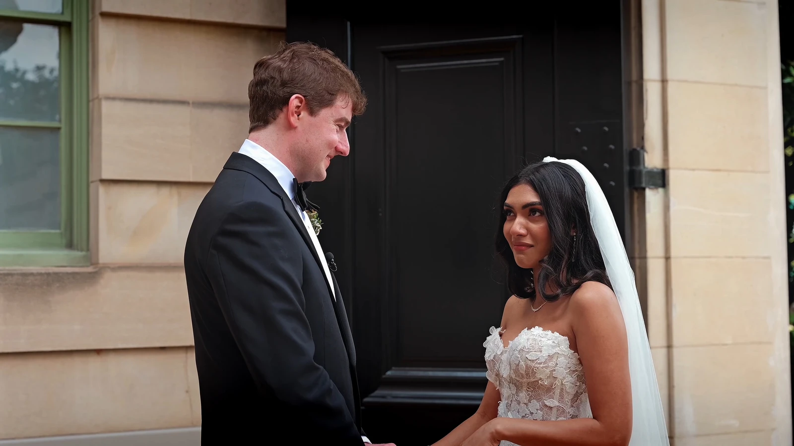 Still from a wedding film: the bride and groom face each other at a doorway before the ceremony
