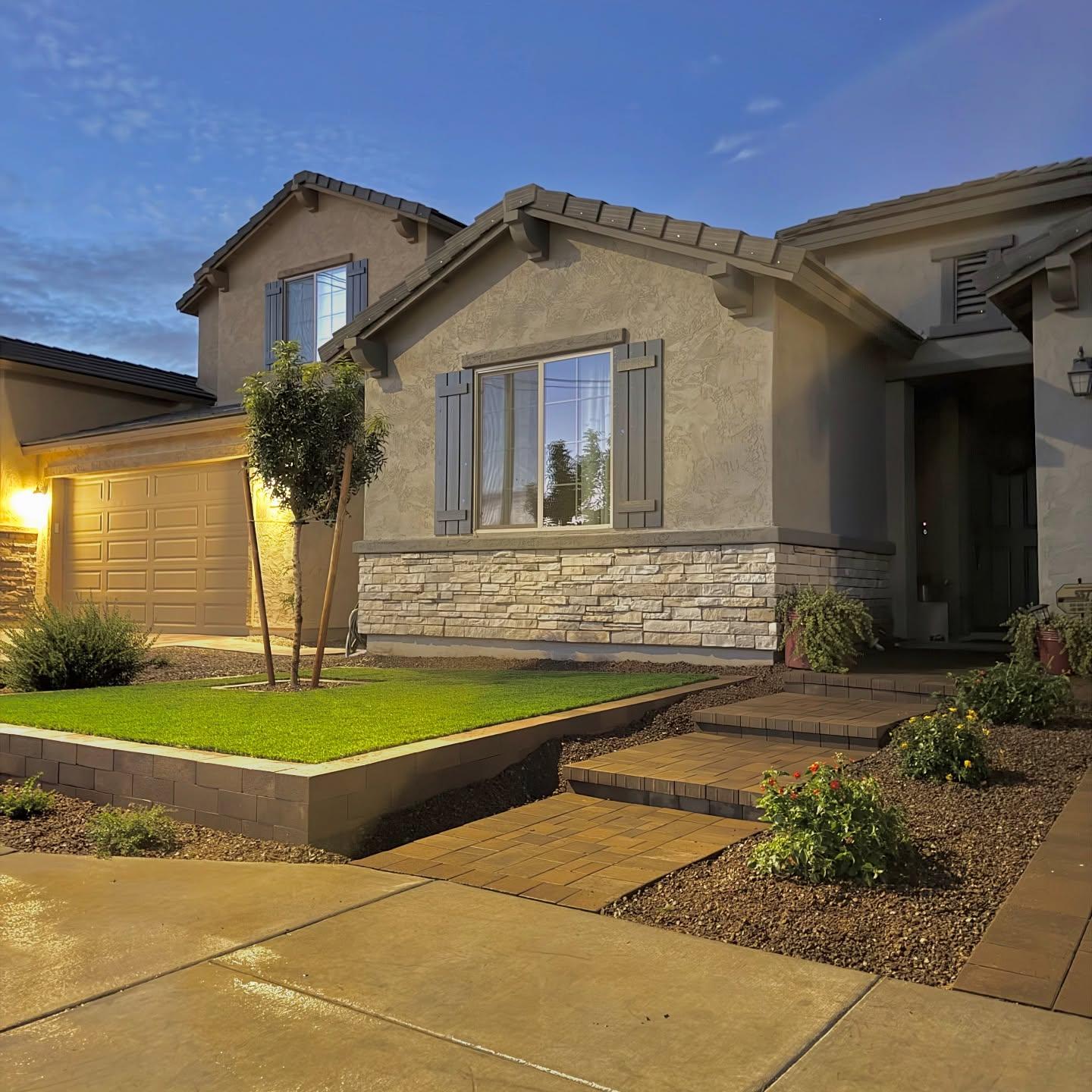 Front exterior at dusk, stone veneer, raised turf planter, and paver steps by AZ Elevate Phoenix